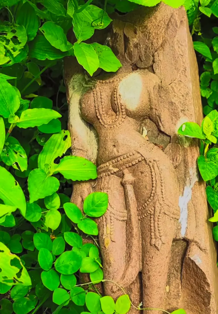 Weathered stone figure among green leaves